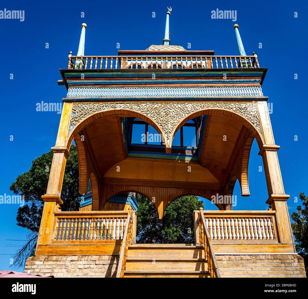 Ein wunderschön verzierter hölzerner Pavillon mit komplizierten Schnitzereien und einem leuchtend blauen Dach vor einem klaren blauen Himmel. Die Strukturkomponenten sind bogenförmig geöffnet Stockfoto