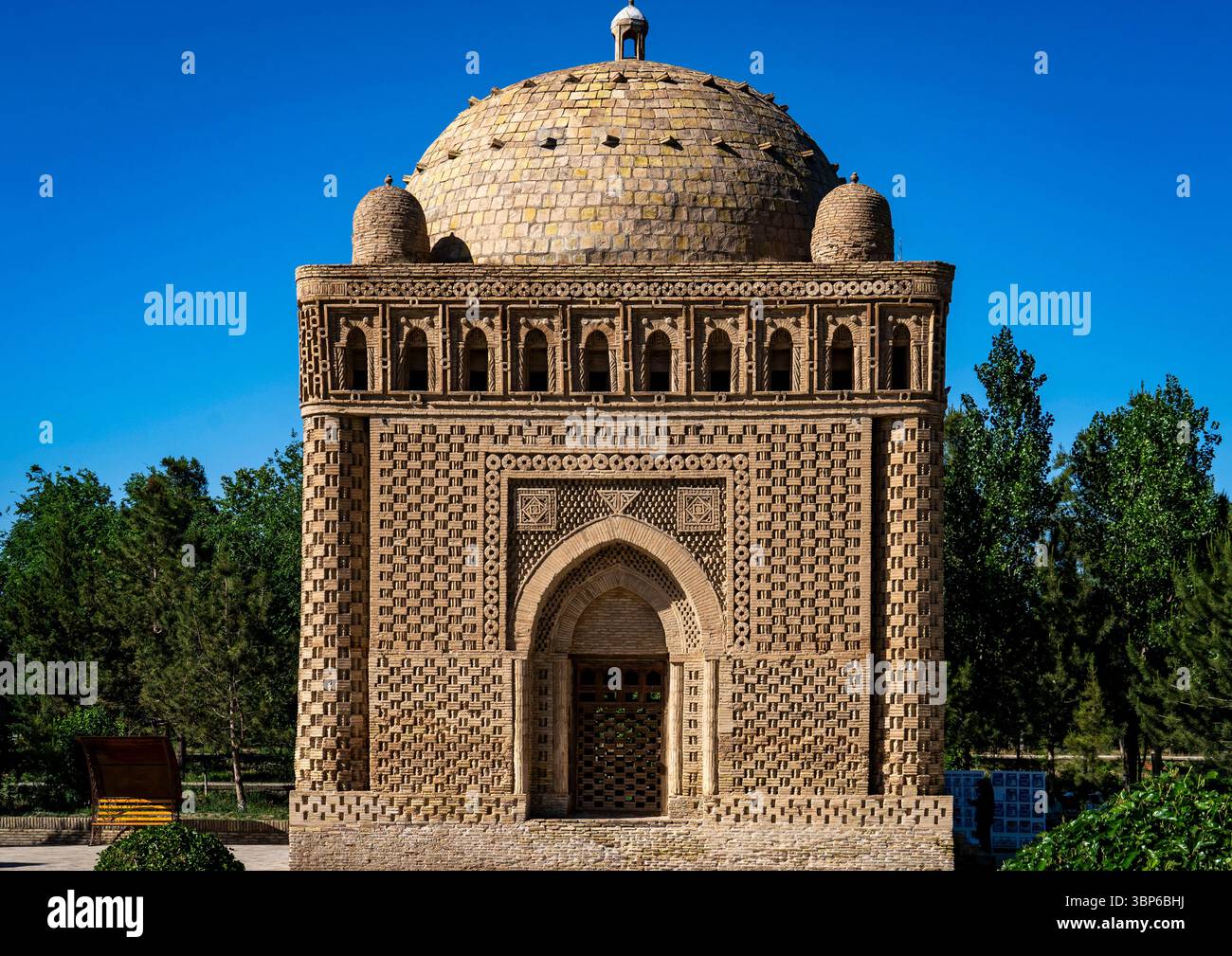 Ein wunderschön gestaltetes historisches Gebäude mit kompliziertem Ziegelwerk und einer Kuppel, umgeben von üppigem Grün unter einem klaren blauen Himmel. Stockfoto