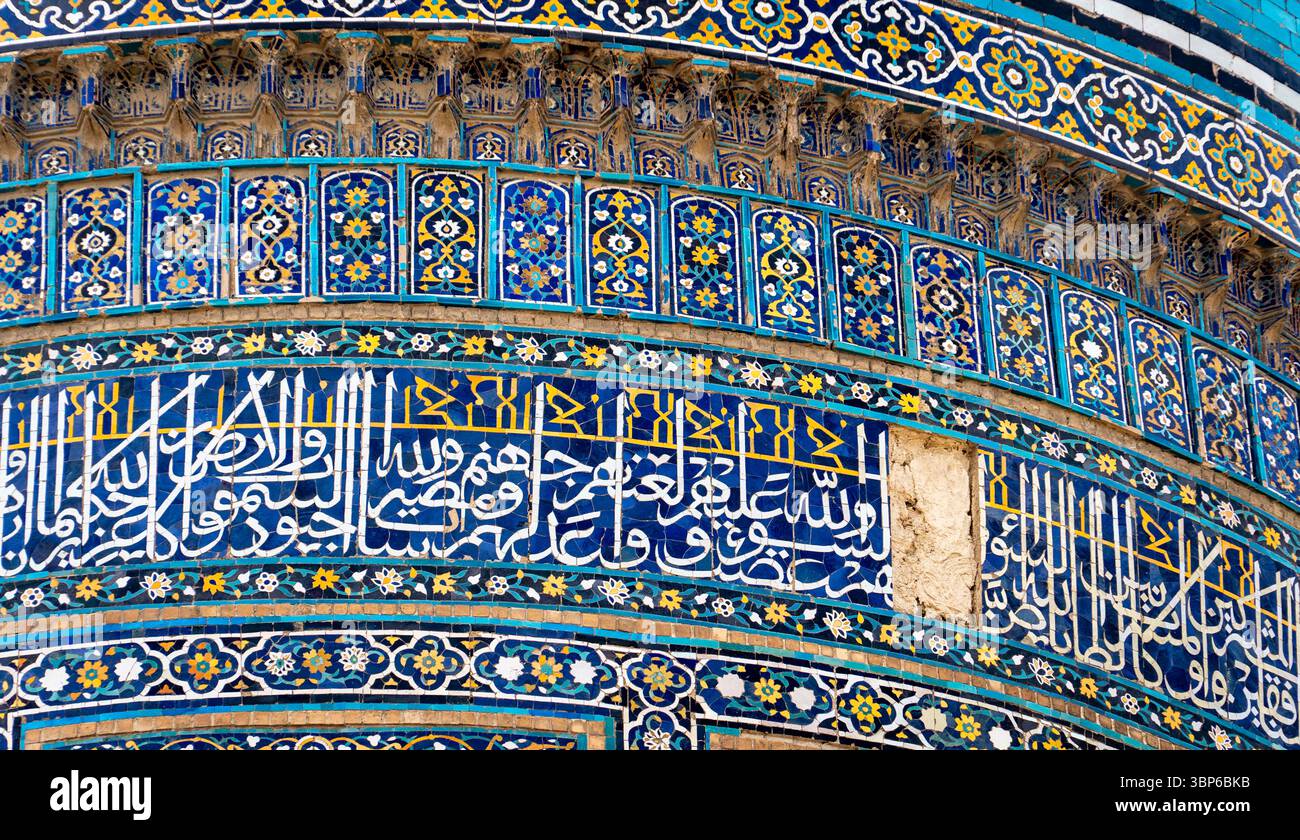 Nahaufnahme komplizierter islamischer Fliesenarbeiten mit bunten geometrischen Mustern und arabischer Kalligraphie. Das Design zeigt leuchtende Blau-, Gelb- und Stockfoto