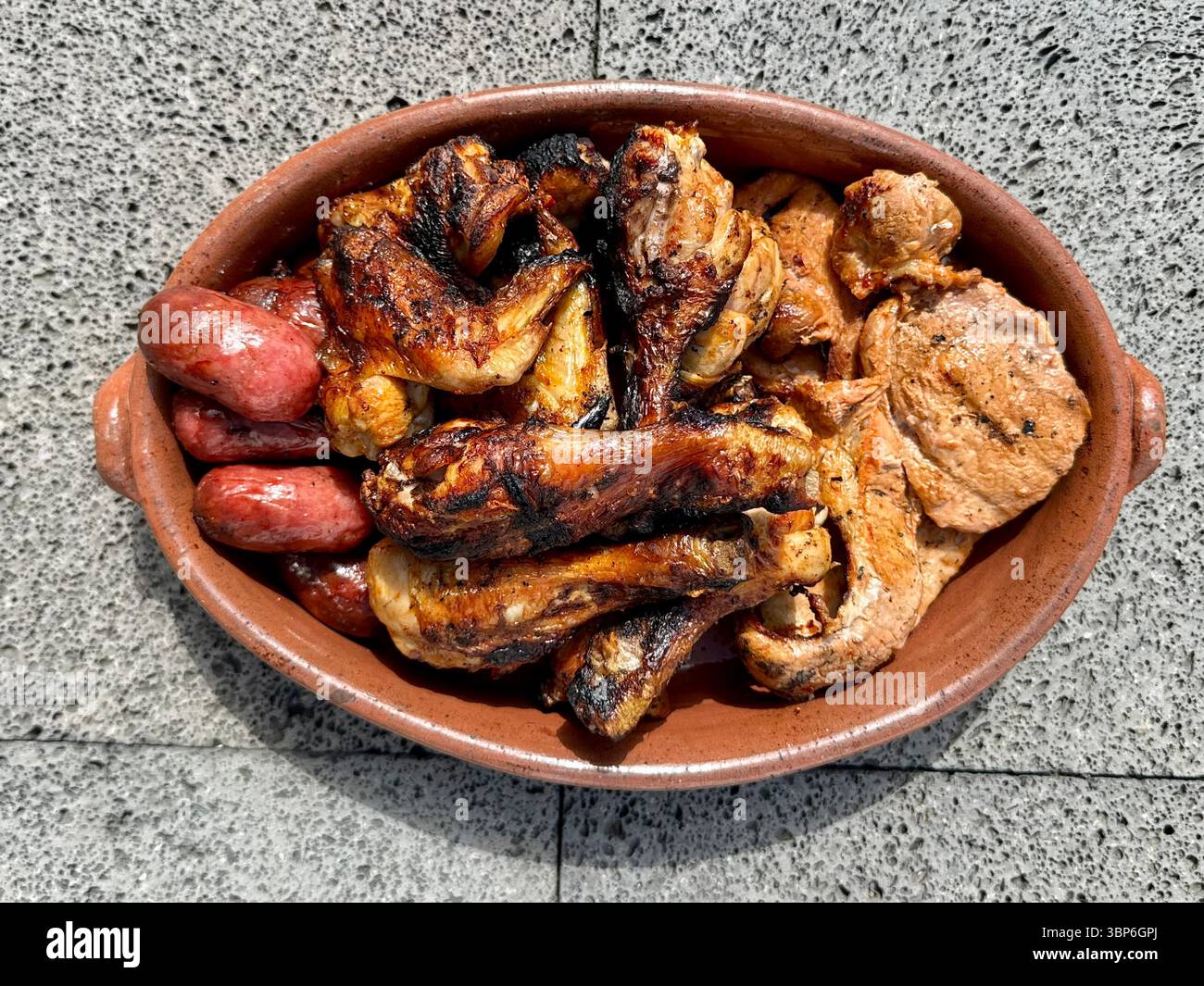 Gemischte gegrillte Fleischplatte, serviert in einer Terrakotta-Form mit Hähnchenflügel, Schweinekoteletts und Würstchen. Stockfoto