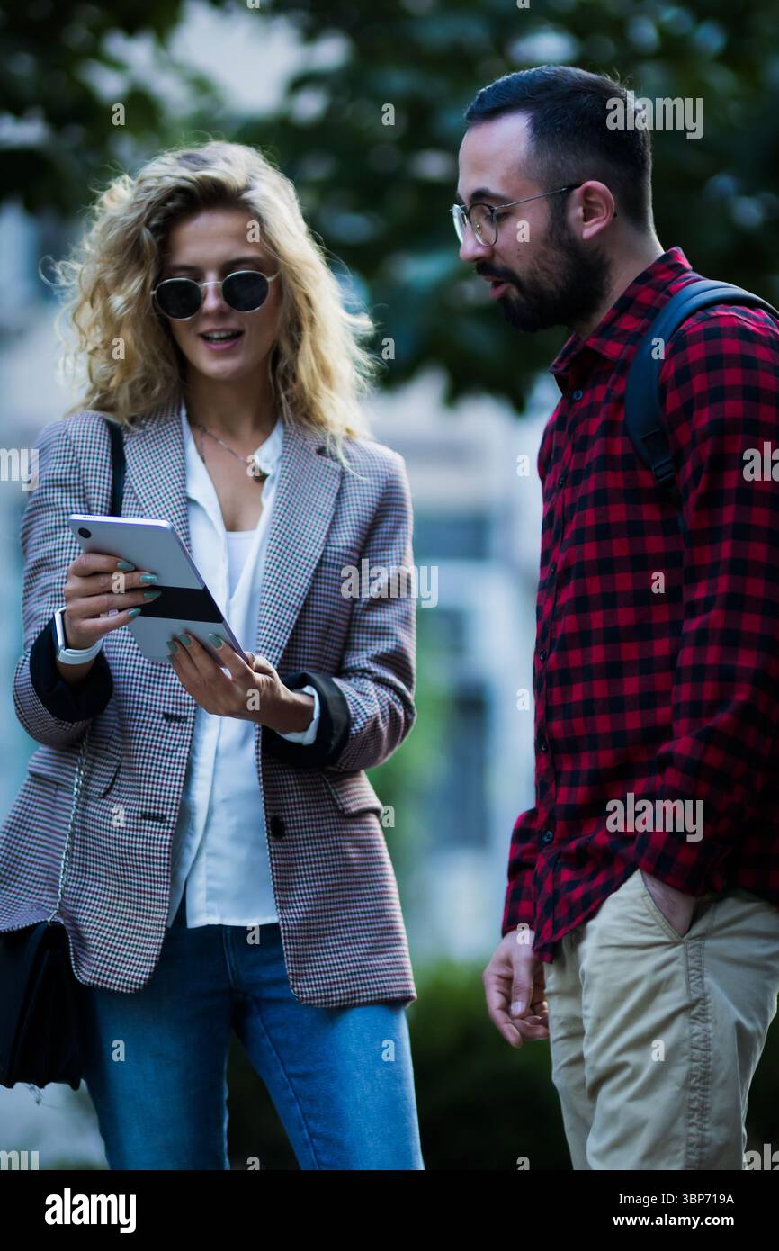 Ein Mann und eine Frau in einer Outdoor-Umgebung, die mit einem digitalen Tablet eine professionelle Diskussion führen und Teamwork und moderne Technologie in einem ungezwungenen Ambiente präsentieren Stockfoto