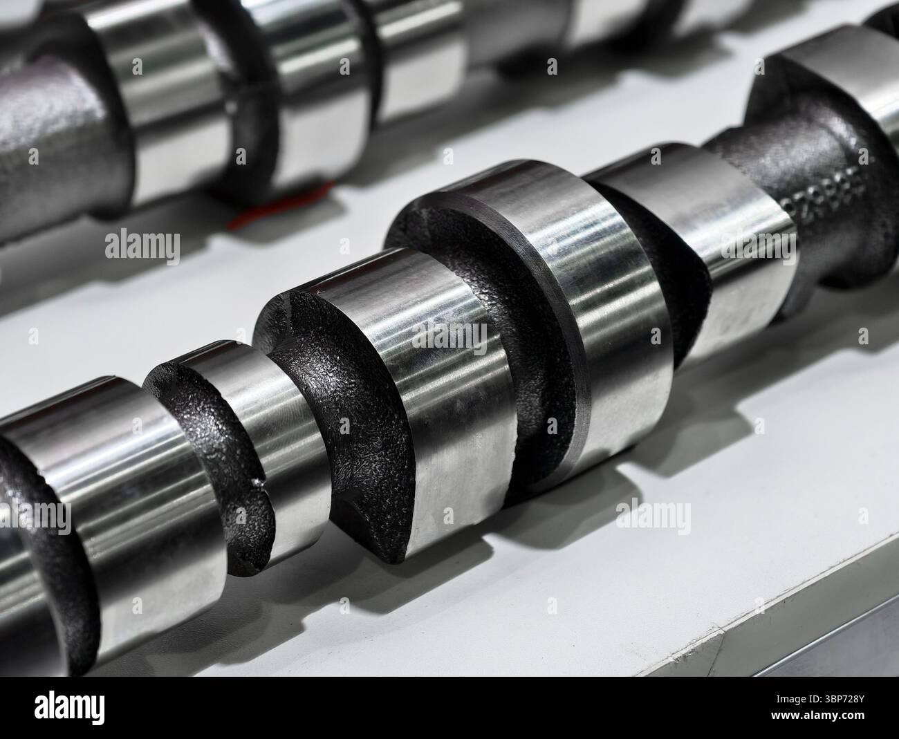 Metallnockenwelle mit polierter Oberfläche, die tagsüber in Werkstattstellung auf einer Oberfläche angezeigt wird Stockfoto