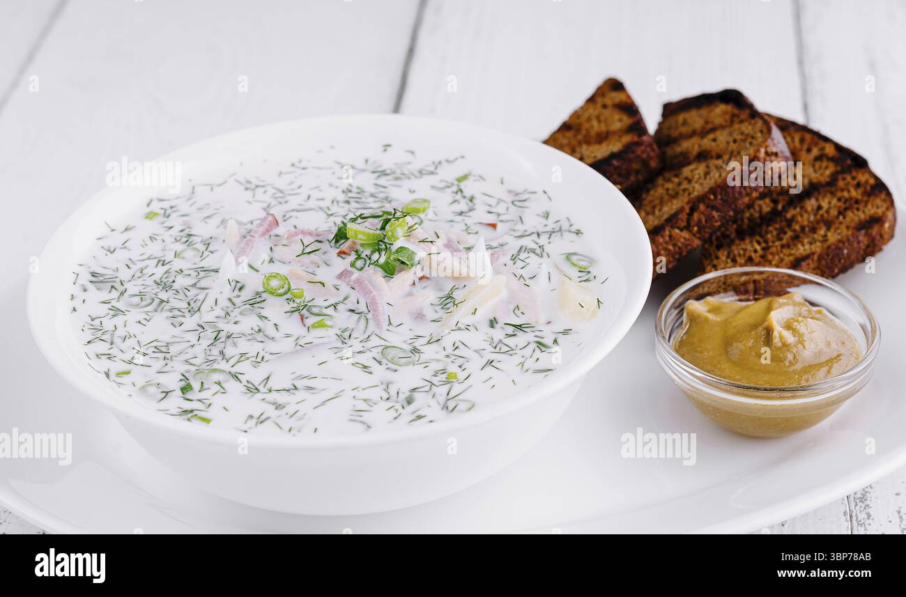 Essen, traditionelle russische kalte Suppe Okroschka, serviert in einer Schüssel mit Roggenbrot und Senf auf weißem hölzernem Hintergrund Stockfoto