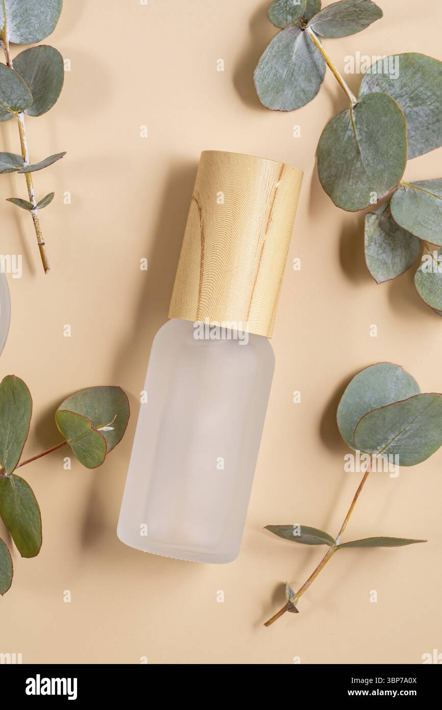 Leere Flasche aus mattem Glas für ätherisches Öl mit Pipette auf beigefarbenem Hintergrund verzierte Eukalyptusblätter. Hautpflegekonzept mit Naturkosmetik Stockfoto