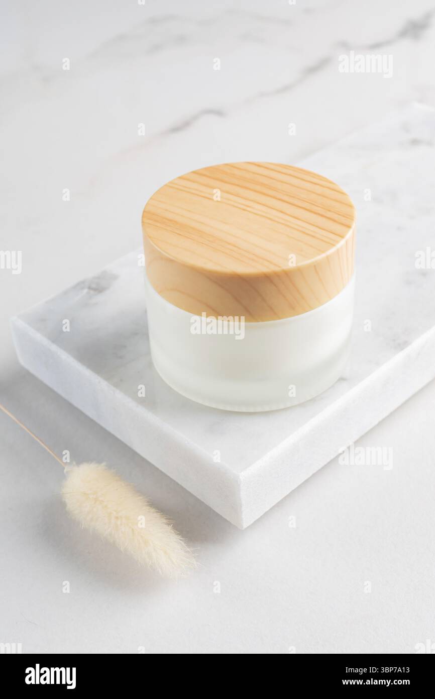 Cremefarbenes Glas auf Marmortablett. Kosmetisches Hautpflegemittel, leere Milchglasverpackung. Weiße Lotion ohne Marke, Balsam, Creme-Mockup. Sonnencreme Flasche wi Stockfoto