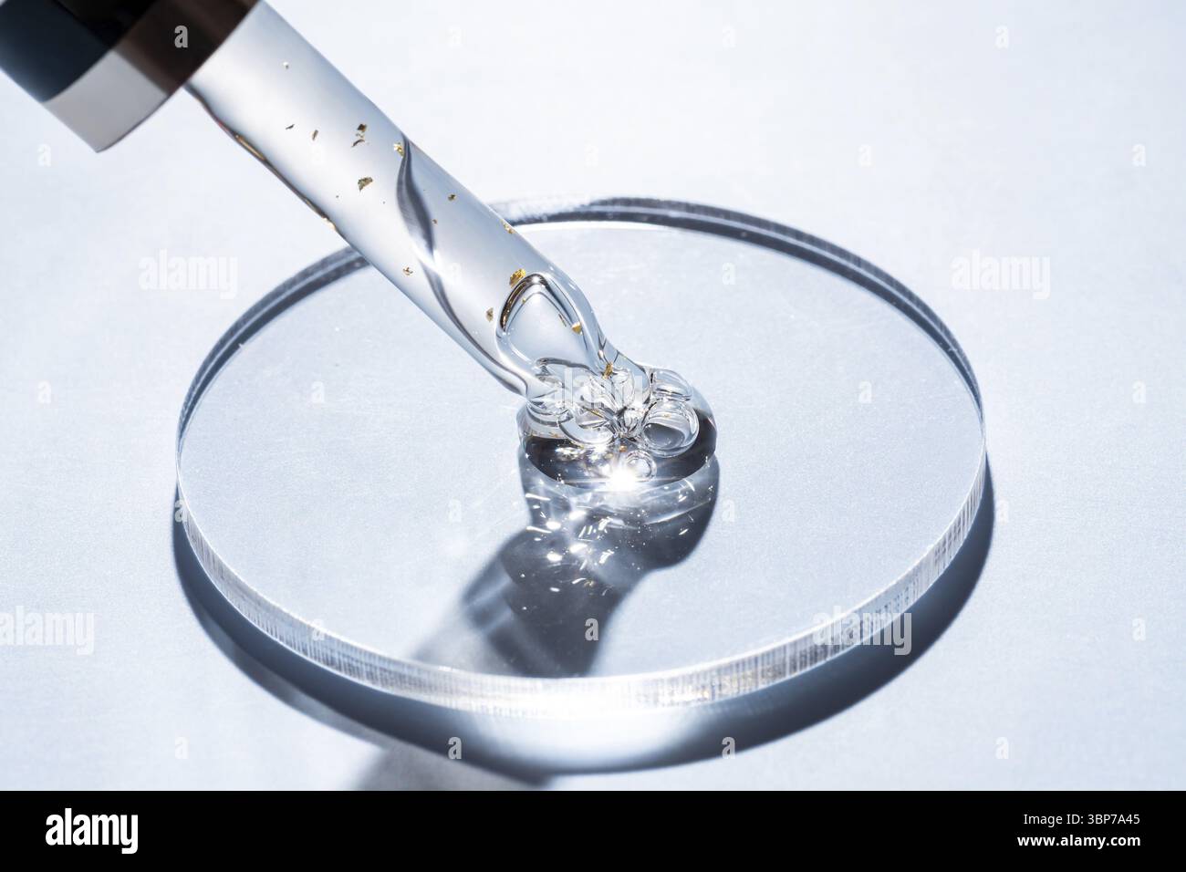 Pipetten mit kosmetischem Gel-Produkt mit Goldpartikeln in Petrischale auf blauem Hintergrund. Hautpflegebabor Stockfoto
