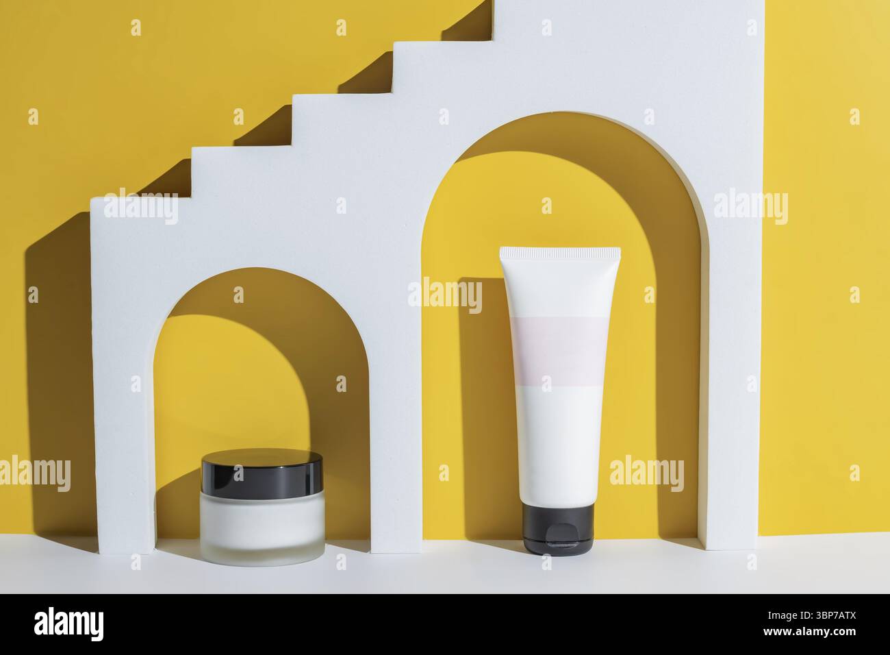 Kosmetische Schönheitsprodukte in weißem Bogen auf gelbem Hintergrund. Verpackung ohne Marke Adv. Cremebecher und -Tube Stockfoto