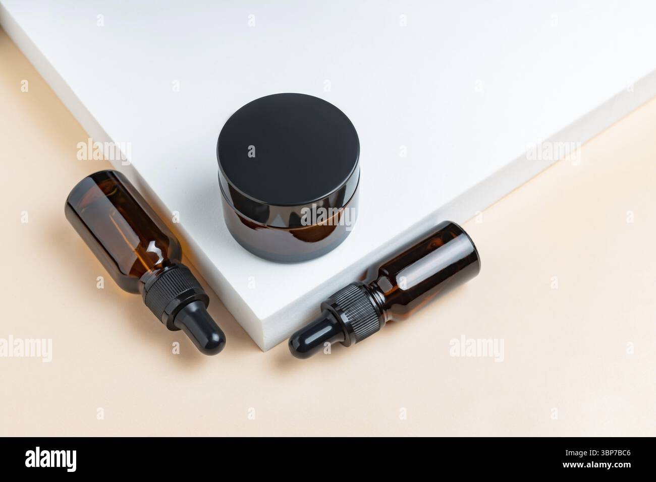 Natürliches Hautpflegeprodukt in Glasflaschen mit Tropf. Serum für Frau Gesichtshaut. Pflanzliche Mineralkosmetik auf weißem Podium. Dunkles Glas-Paket kosmet Stockfoto