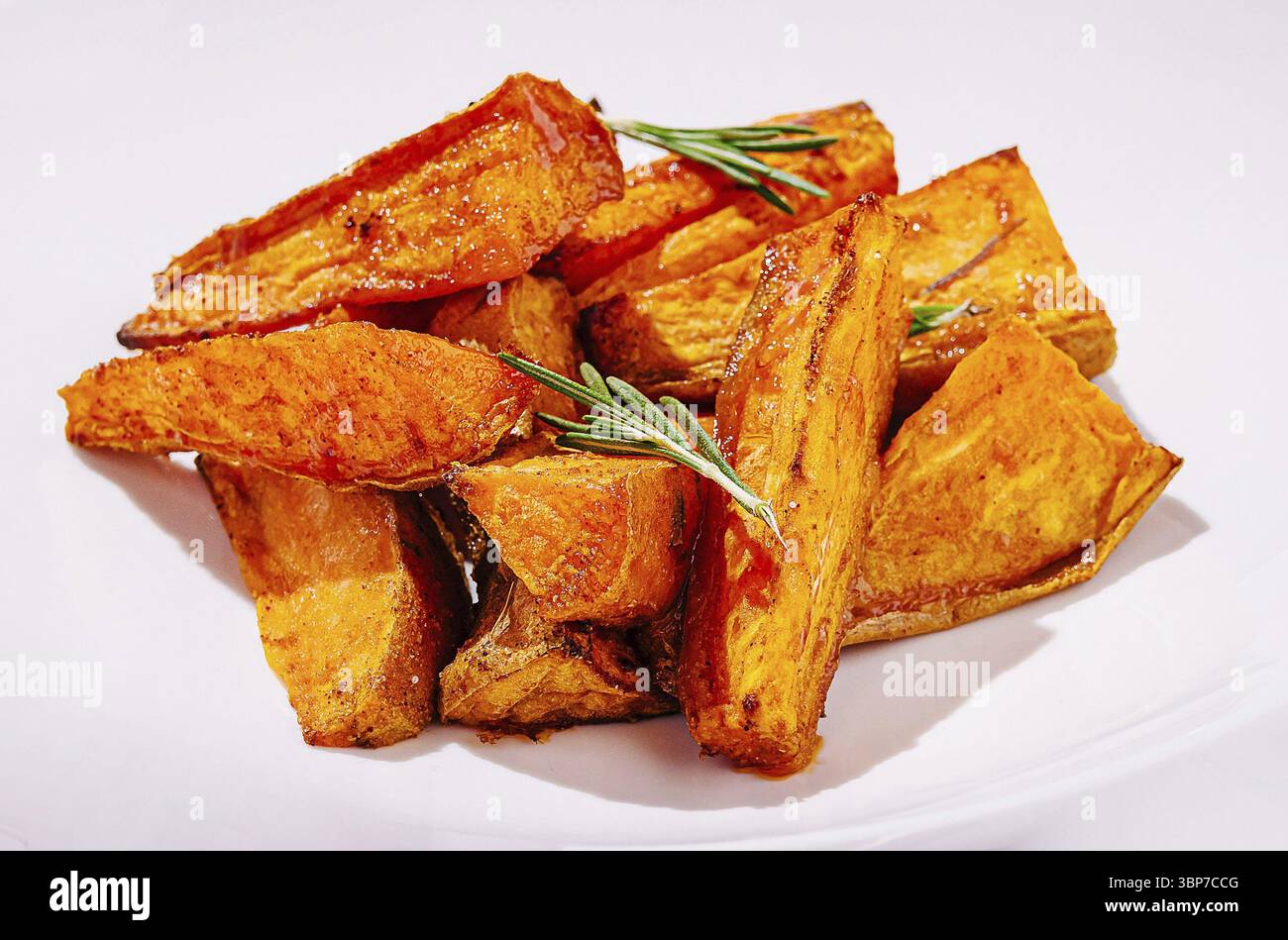 Speisen, goldbraun geröstete Süßkartoffeln werden auf einem einfachen weißen Teller präsentiert, garniert mit frischen Rosmarinzweigen, die ihr knuspriges Textu hervorheben Stockfoto