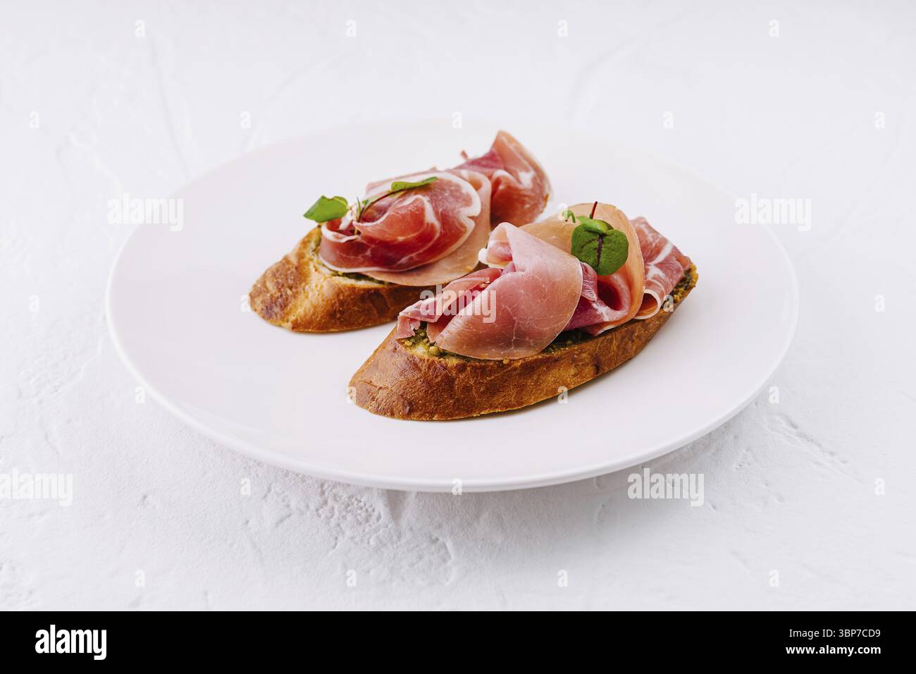 Essen, Gourmet Bruschetta mit Schinken und Basilikum auf einem sauberen Teller vor weißem Hintergrund Stockfoto