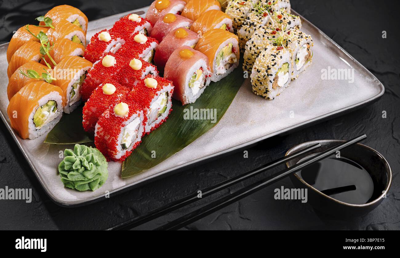 Essen, verschiedene Sushi-Brötchen kunstvoll mit Garnituren auf schwarzem Hintergrund Stockfoto