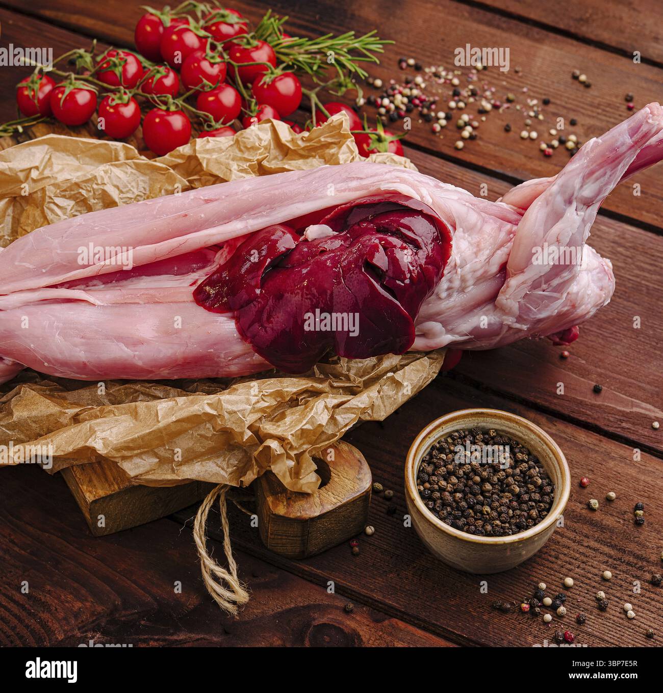 Essen, frisch zubereitetes Kaninchenfleisch wird neben Kirschtomaten und grünen Kräutern präsentiert. Die satten Farben und Texturen schaffen eine einladende Atmosphäre Stockfoto