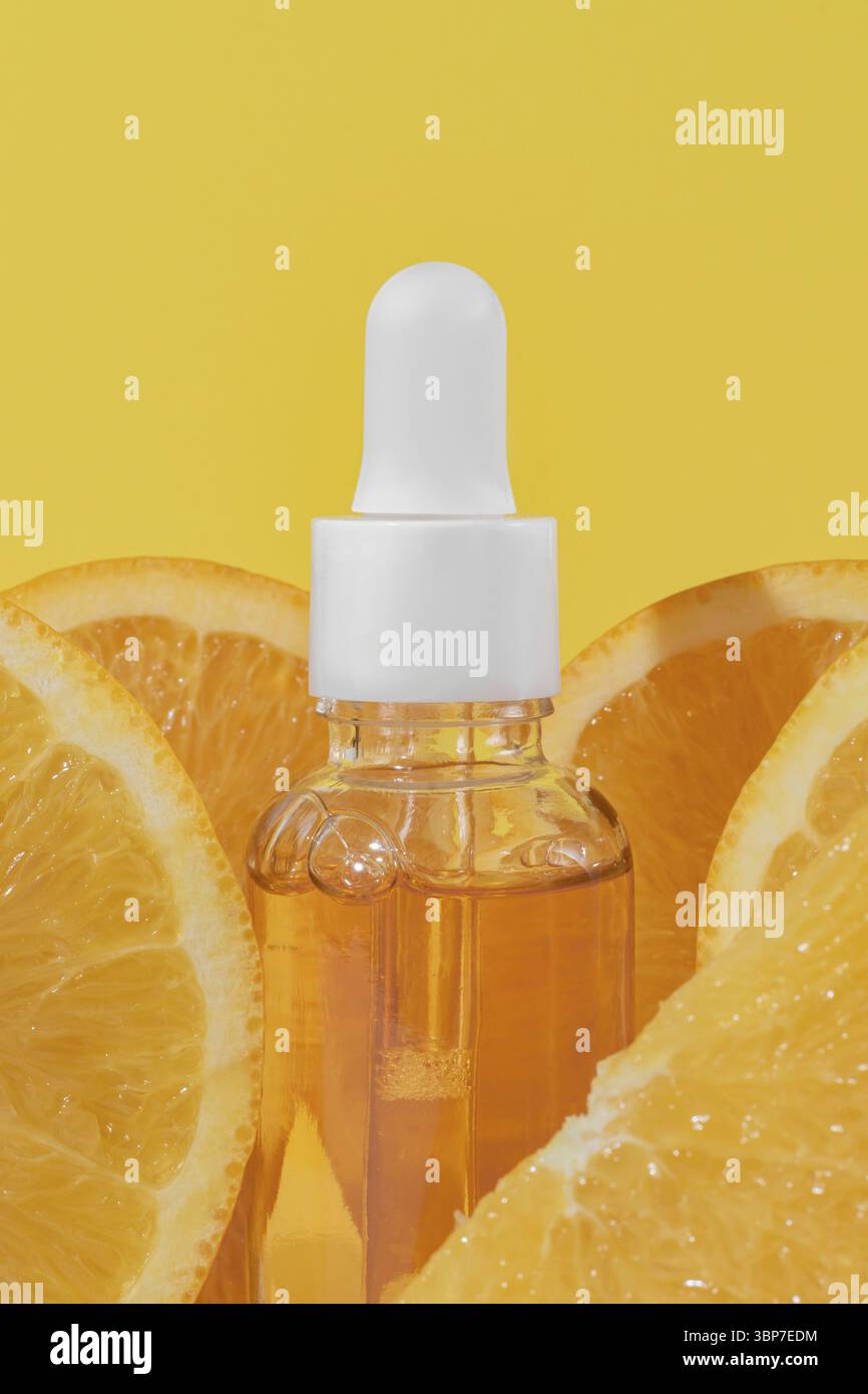 Leuchtend gelber Hintergrund mit einer Tropfflasche für ein Gesichtsserum mit Zitrusfruechten, das Vitamin C und frische Orangenscheiben enthaelt, di Stockfoto