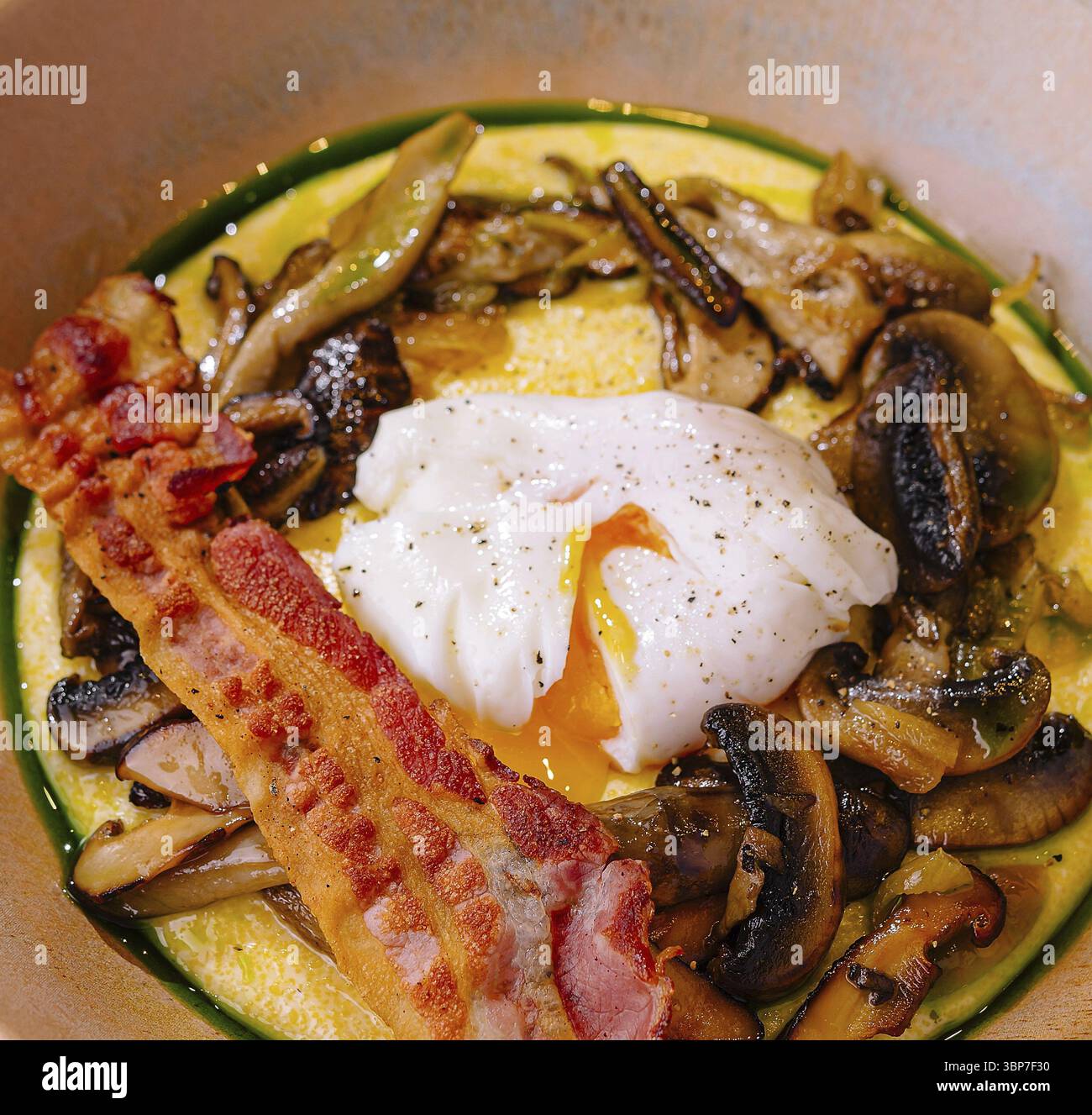Essen, herzhaftes Gericht mit einem pochierten Ei, knusprigem Speck und sautierten Pilzen auf einem Pastellteller Stockfoto