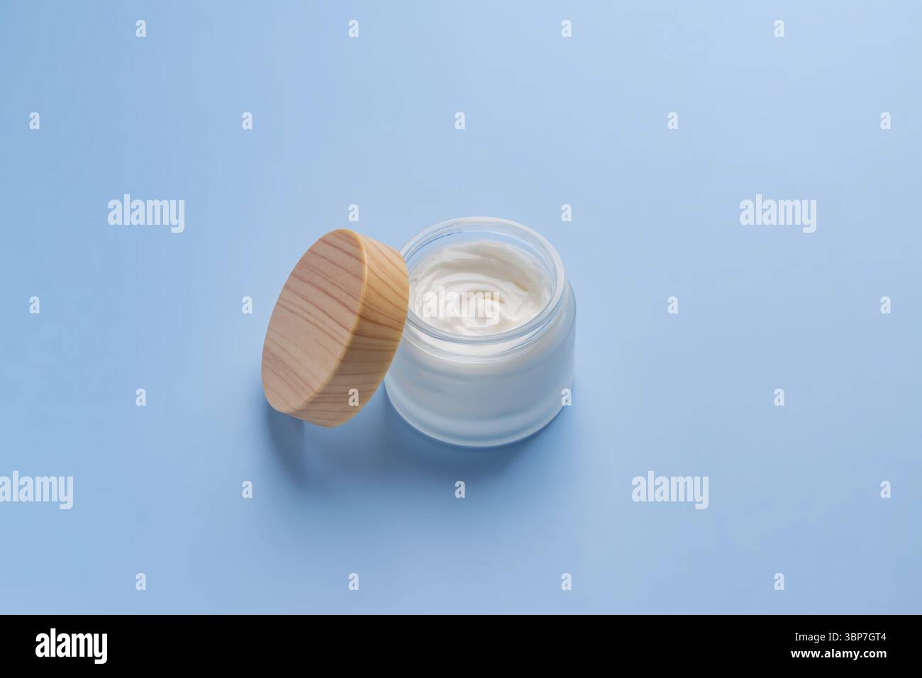 Gesichtscreme auf blauem Hintergrund. Professioneller Milchglasbehälter mit Bambusdeckel für Gesichts- und Körperbehandlungen. Paket ohne Branding, Modell Stockfoto