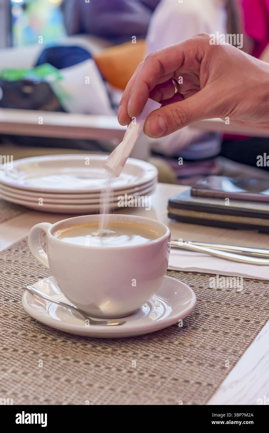 Eine Hand Zugabe von Zucker in eine Tasse schwarzen Kaffee Stockfoto