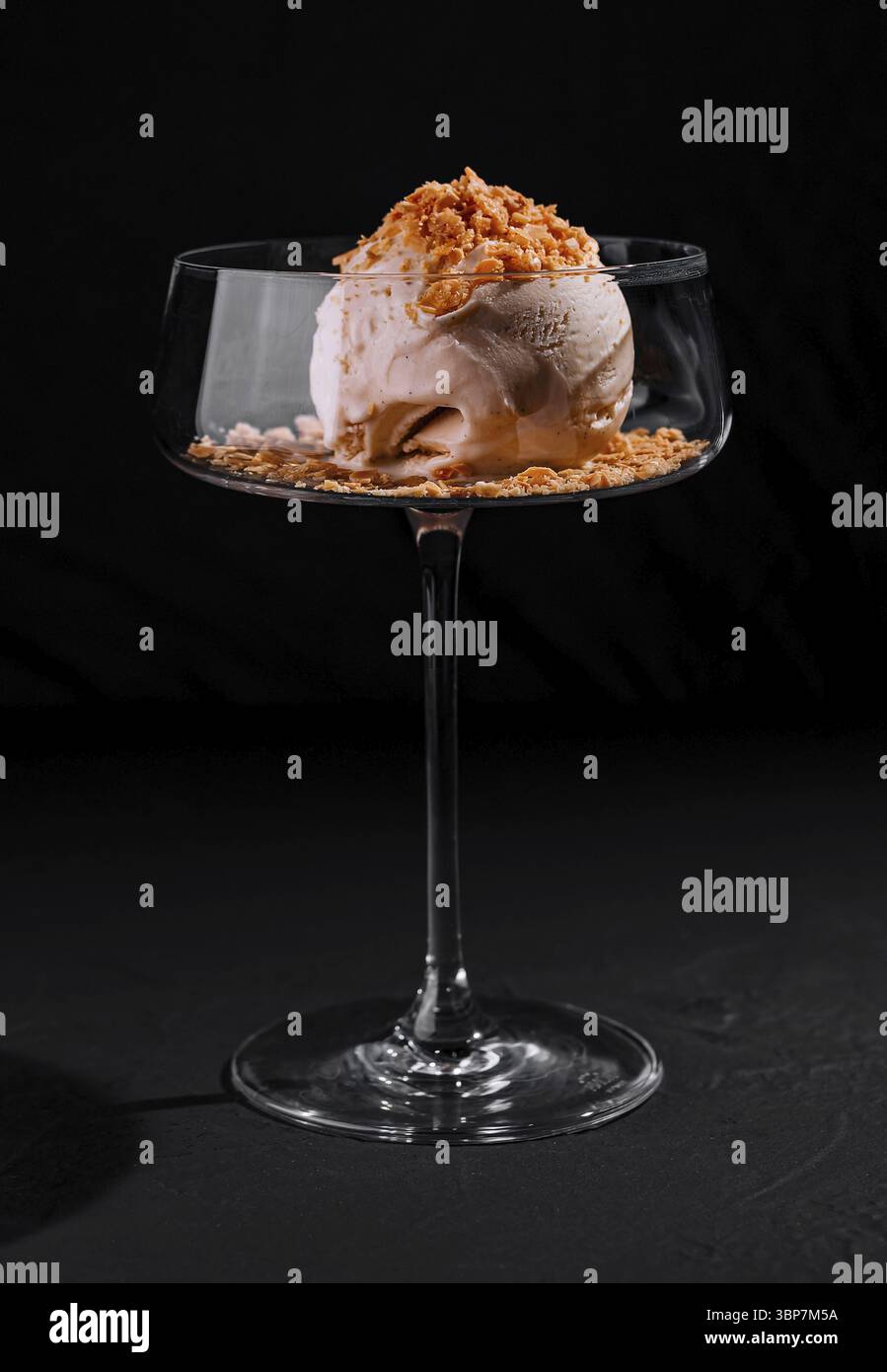 Essen, kunstvoll überzogenes Eis Dessert mit Crumble Belag in einem stilvollen Coupé Glas auf dunklem Hintergrund Stockfoto