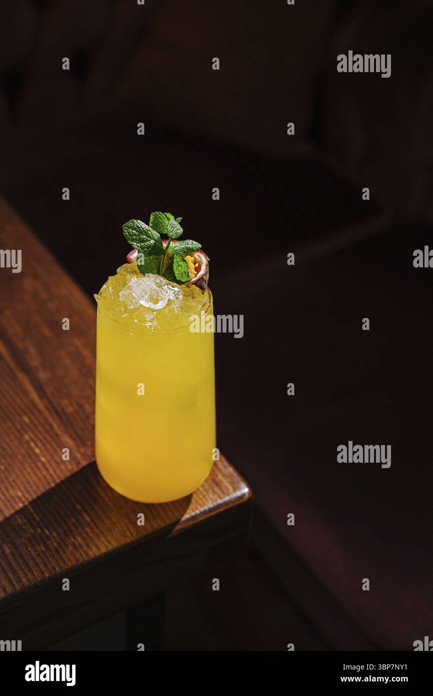 Das Essen, Ein lebendiger tropischer Cocktail, gefüllt mit Eis und garniert mit frischer Minze, liegt auf einem polierten Holztisch in einer warmen, einladenden Atmosphäre, per Stockfoto