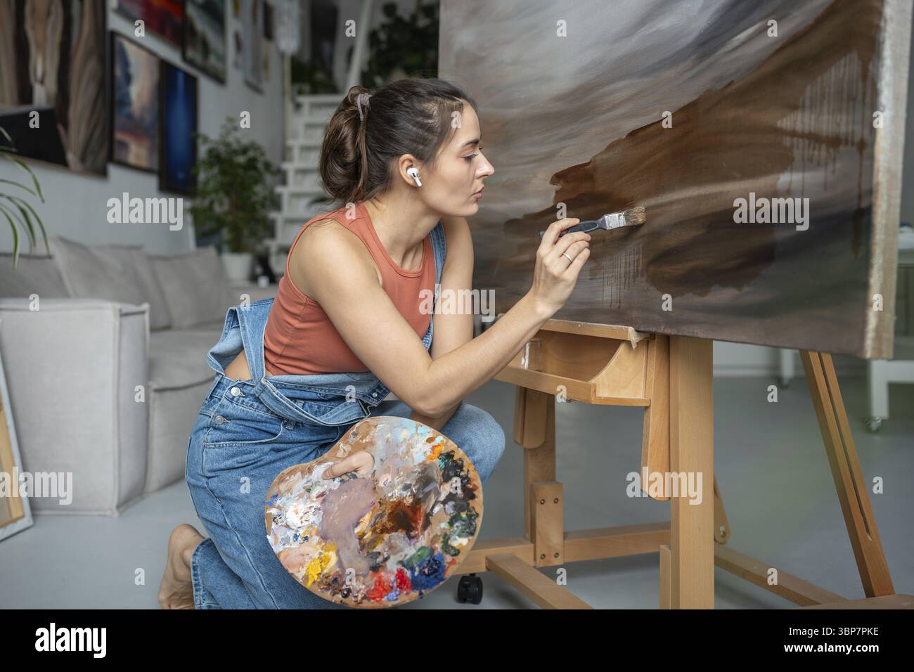 Begabte seriöse Künstlerin, die mit sanften Pinselstrichen an moderner abstrakter Malerei arbeitet. Mädchen, das dunkle impressionistische Bilder erzeugt Stockfoto