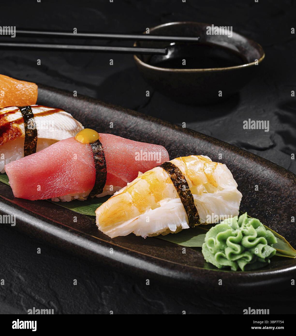 Essen, exquisite Auswahl an Nigiri-Sushi, serviert auf einem schwarzen Teller mit Sojasauce und Essstäbchen Stockfoto