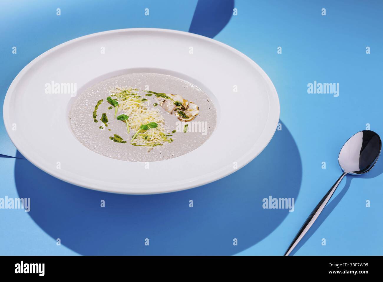 Food, Eine wunderschön präsentierte Schüssel mit cremiger Suppe mit zarten Garnituren und auf einer leuchtend blauen Oberfläche. Das Gericht zeigt kulinarische Kunst Stockfoto