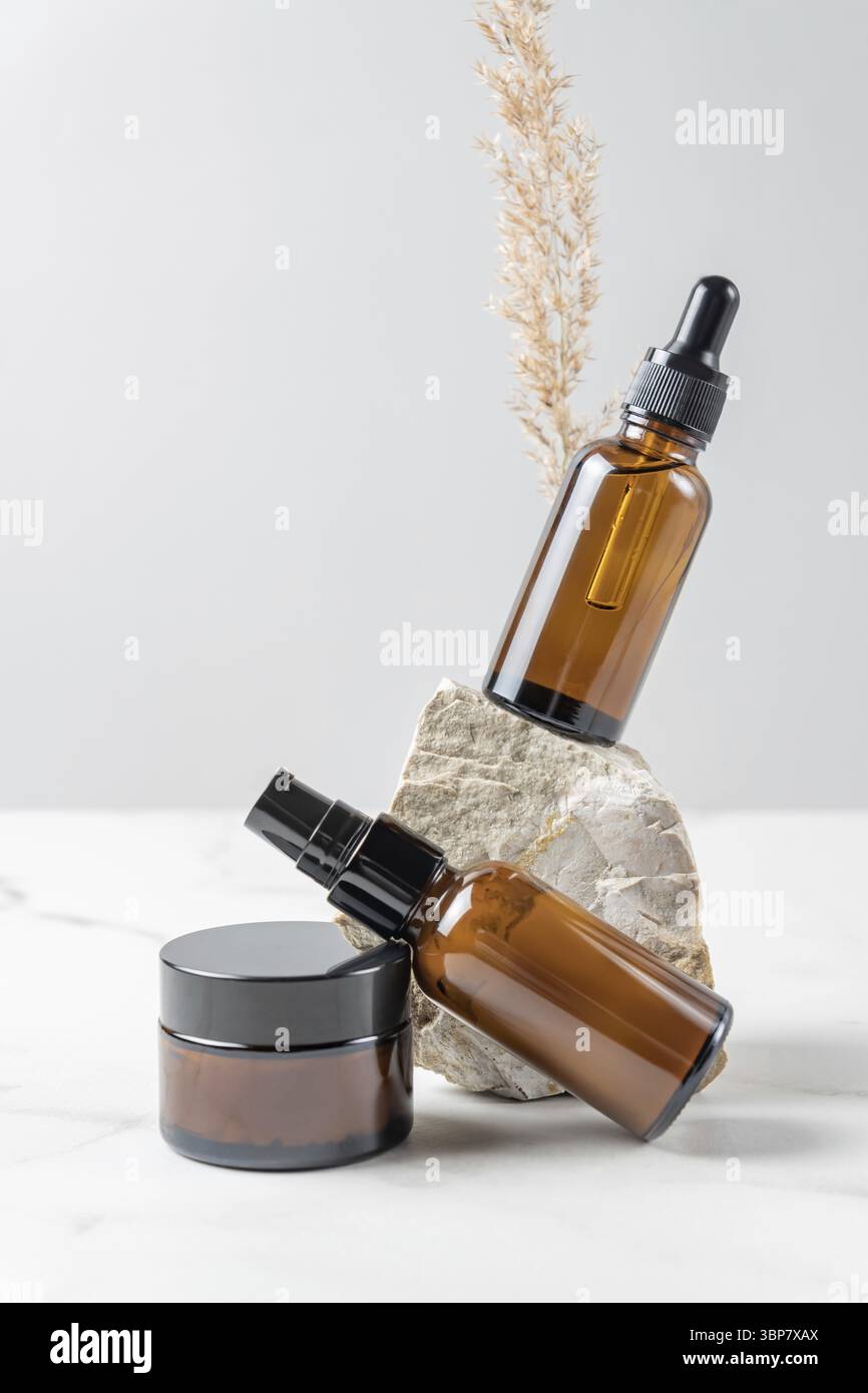 Leere Kosmetikflaschen mit Creme, Feuchtigkeitscreme oder anderen kosmetischen Produkten, Steinen, getrocknete Pflanzenblumen auf grauem Hintergrund. Natürliche Bio-Spa-Kosmetik Stockfoto
