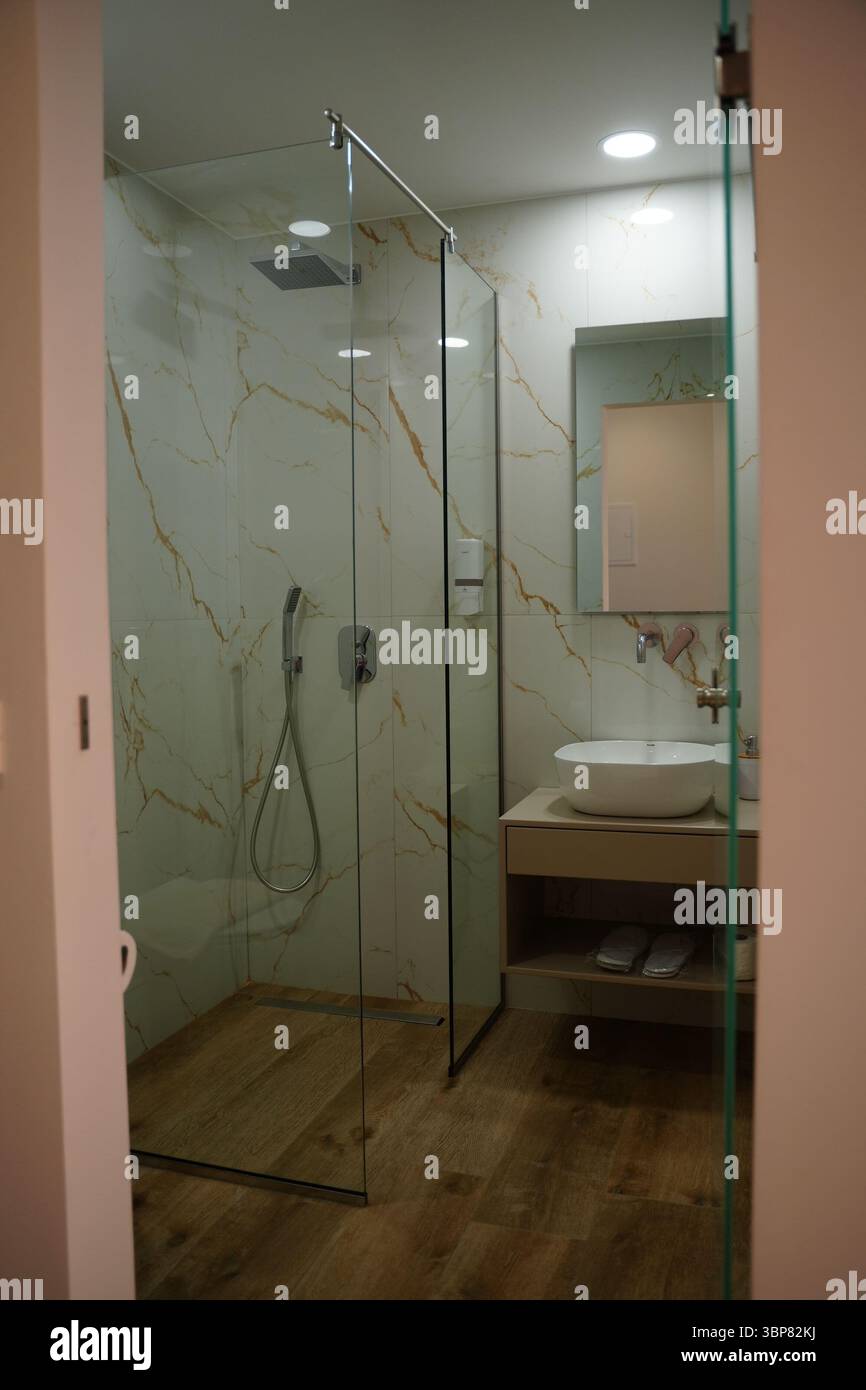 Modernes Bad mit Glasdusche, eleganten Marmorwänden und Holzfußboden. Mit stilvollem Waschbecken und Stockfoto