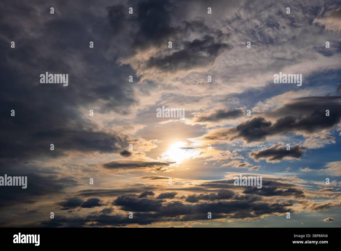 Dramatischer Himmelhintergrund bei Sonnenuntergang mit Sonne, die durch stürmische Wolken scheint. Stockfoto