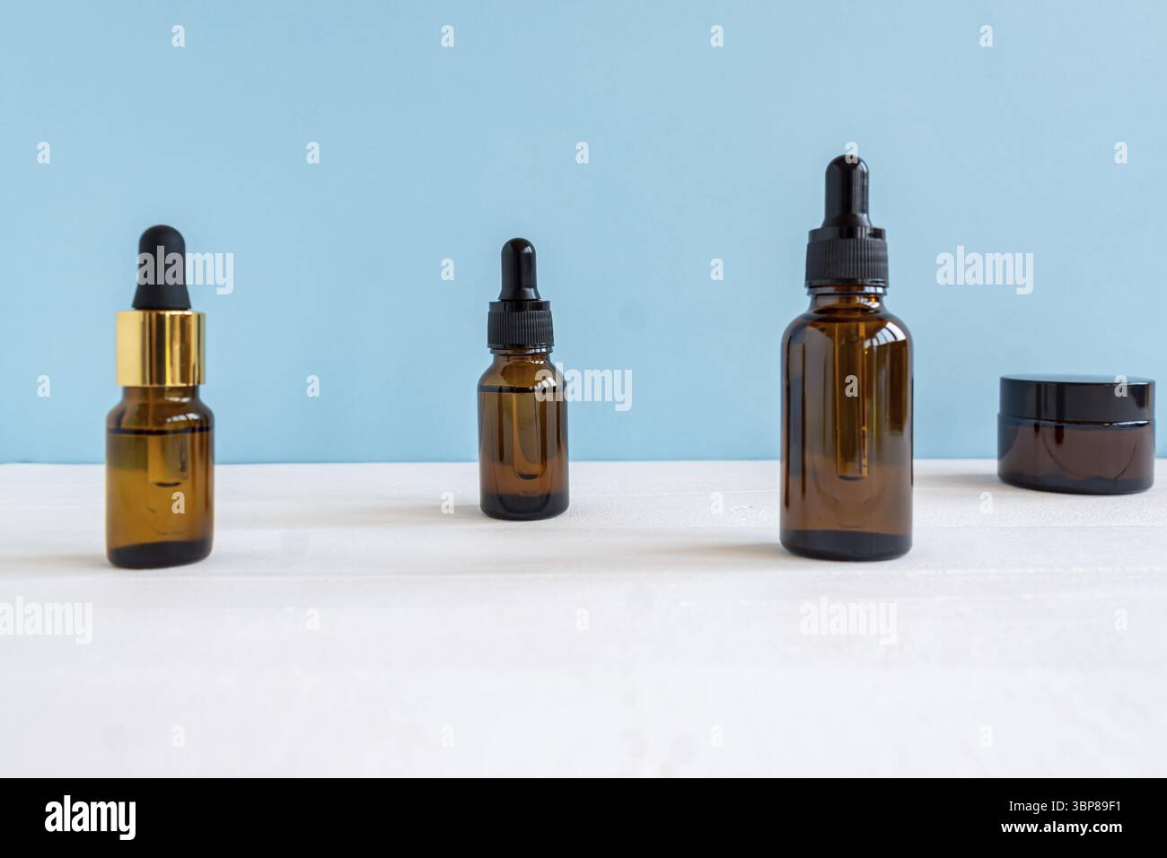 Dunkle Glas- und transparente Kosmetikflaschen mit Gesichts-Serum oder essentioalem Öl auf blauem Hintergrund. Kosmetikprodukte von Unbradned Beauty Stockfoto