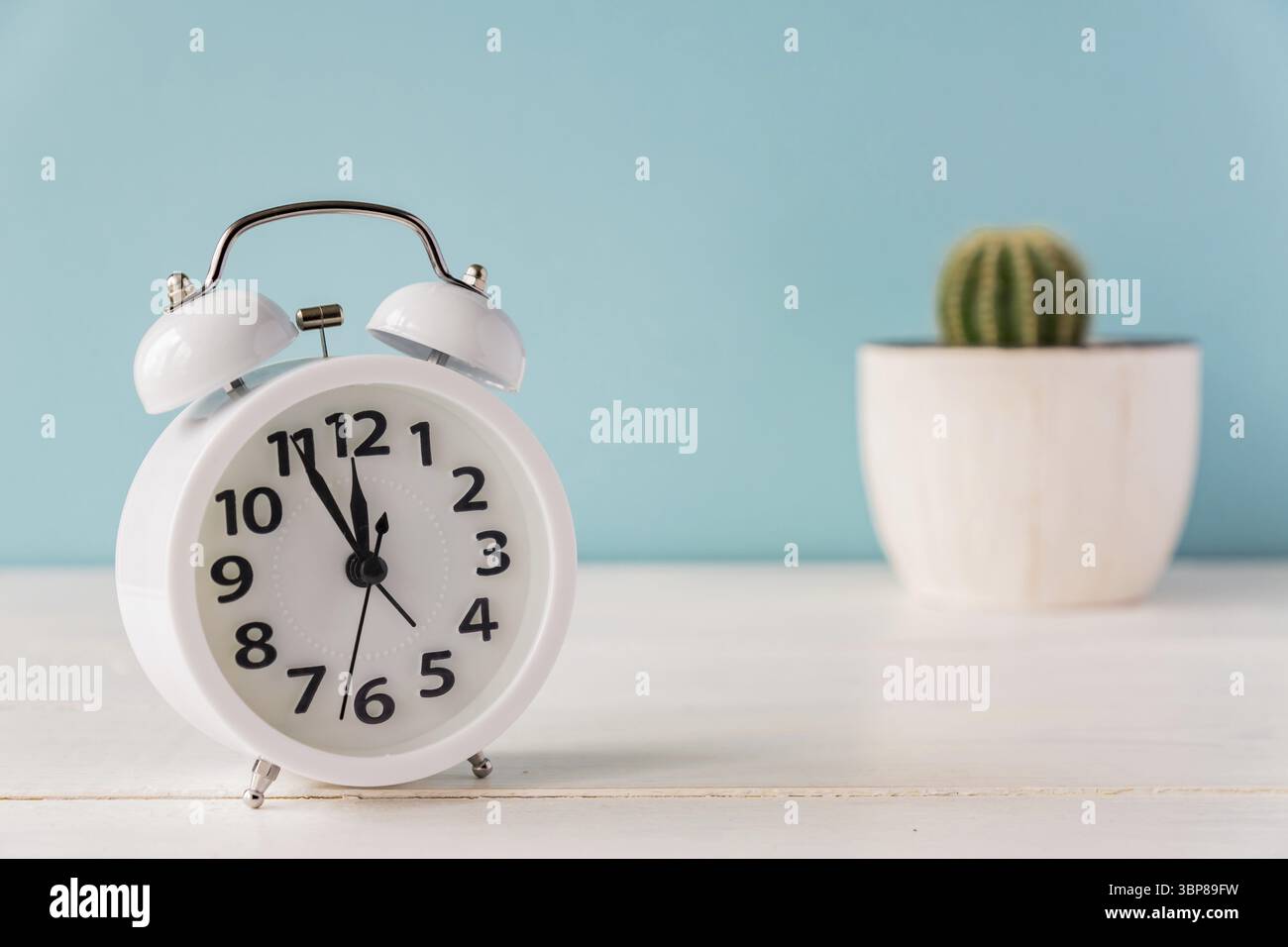 Weißer Wecker steht auf einem Holzregal auf grüner Kulisse. Kaktus in einem Topf auf dem Hintergrund Stockfoto