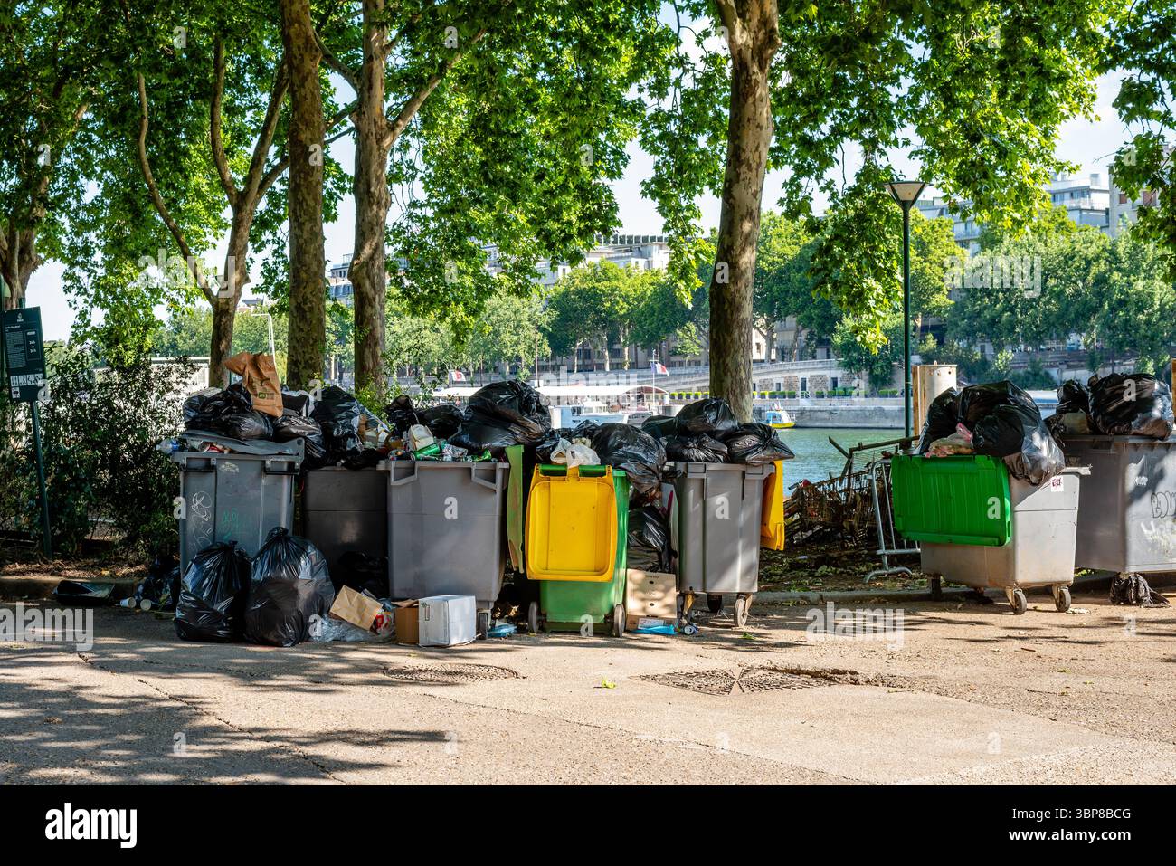Überfüllte Müllcontainer am Ufer der seine. Schwarze Müllsäcke auf dem Boden und Müll verteilen sich um Recyclingbehälter Stockfoto