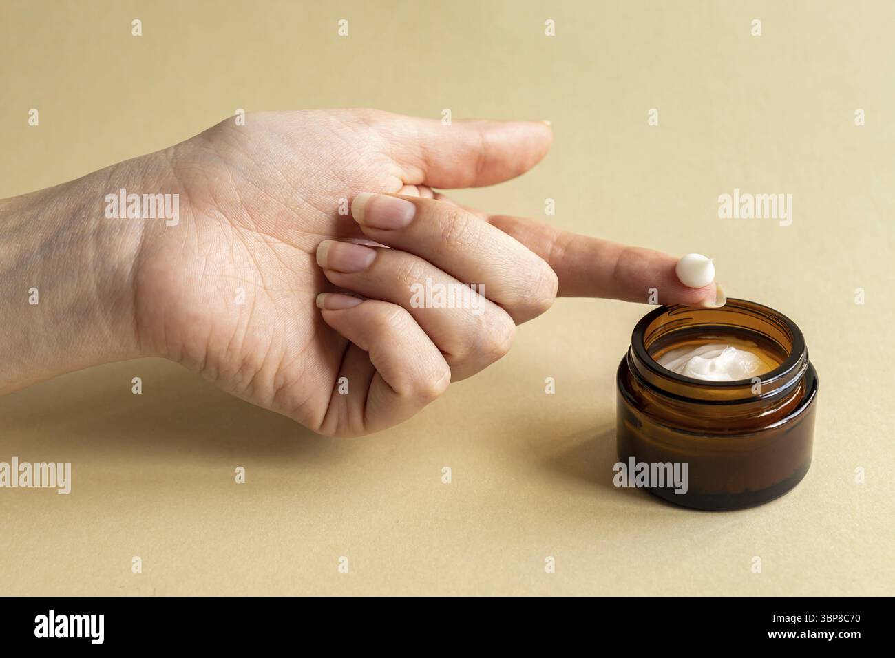 Weibliche Hand berühren unbranded dunklen Glas mit Gesicht mourstabilizing Creme. Flasche für professionelle Kosmetikprodukte. Konzept für Hautpflege und Schönheit. Mo Stockfoto
