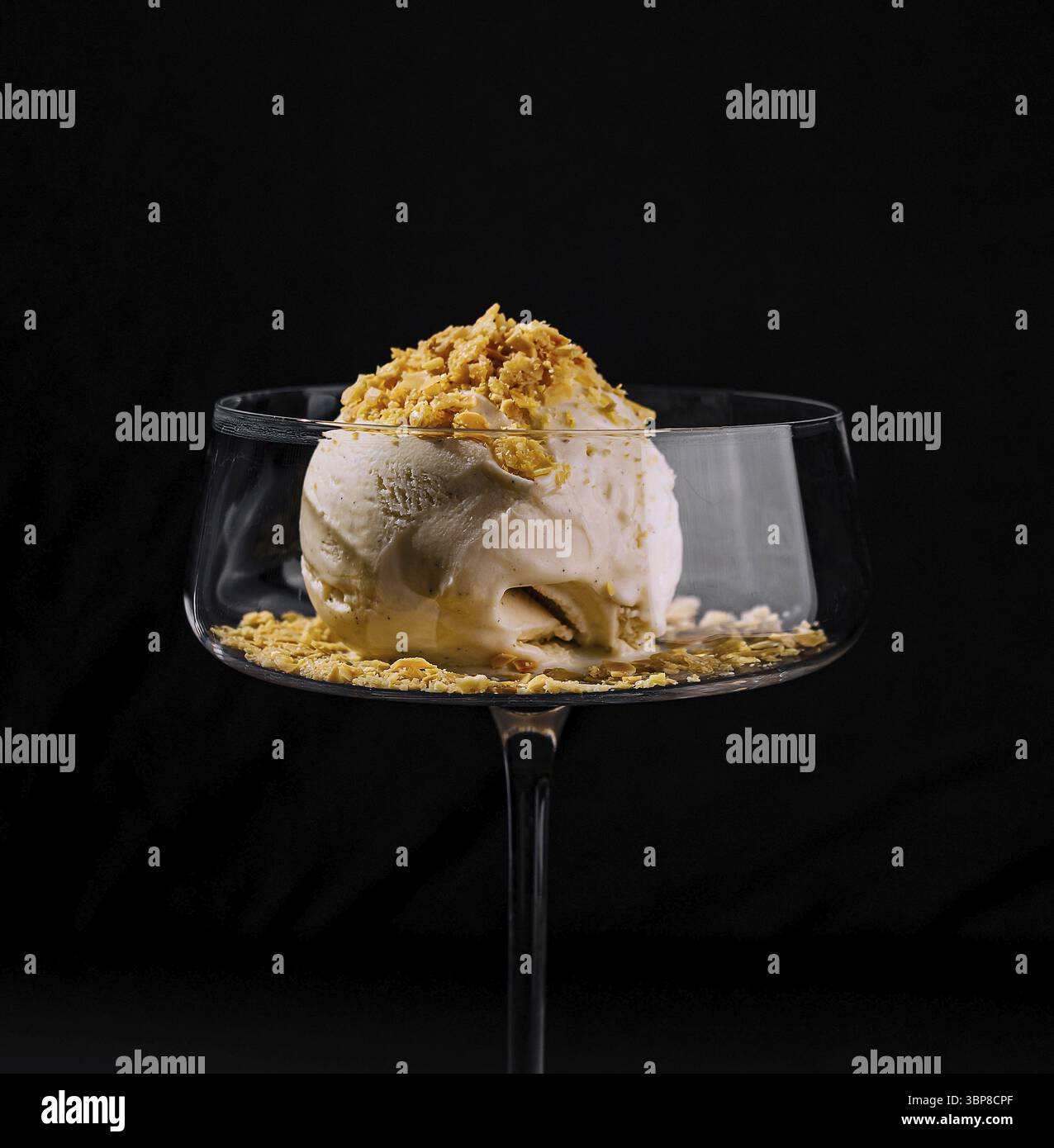 Essen, kunstvoll überzogenes Eis Dessert mit Crumble Belag in einem stilvollen Coupé Glas auf dunklem Hintergrund Stockfoto
