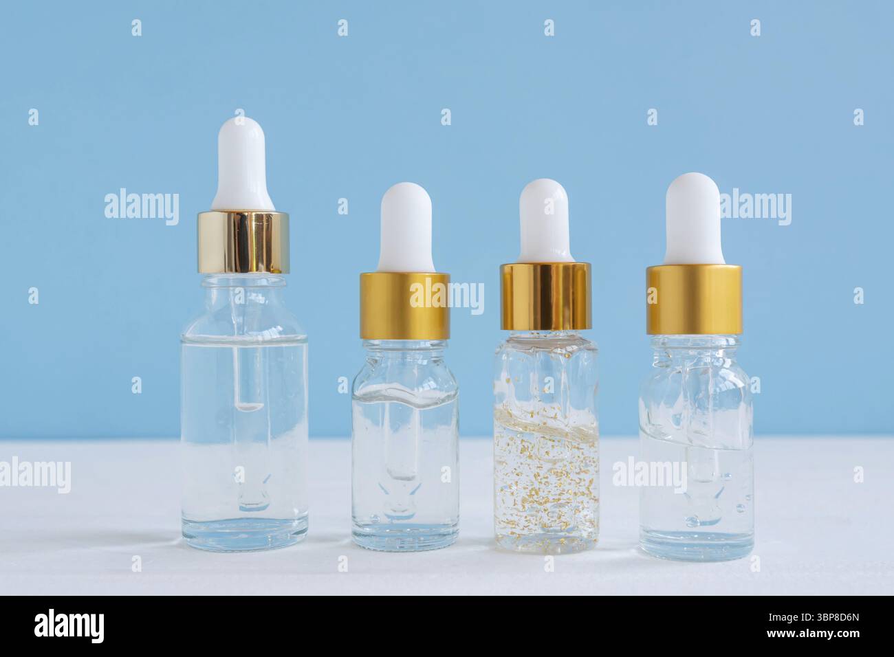 Dunkle Glas- und transparente Kosmetikflaschen mit Gesichts-Serum oder essentioalem Öl auf blauem Hintergrund. Kosmetikprodukte von Unbradned Beauty Stockfoto