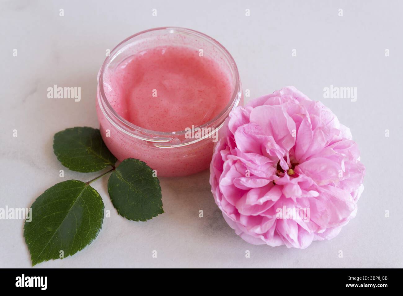 Hygienebad-Produkt. Körper, Gesichts-Rosenpeeling mit blühenden rosa Rosenblüten auf Marmorhintergrund. Wellness-Therapie-Regeneration und Hautpflegekonzept Stockfoto