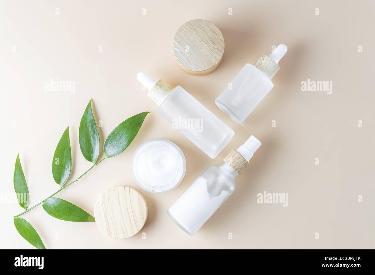 Feuchtigkeitscreme, Serum in Glasflasche und Toner mit grünen Blättern auf beigem Hintergrund. Flach liegend, Draufsicht. Set für Haut- und Körperpflege Beauty PR Stockfoto
