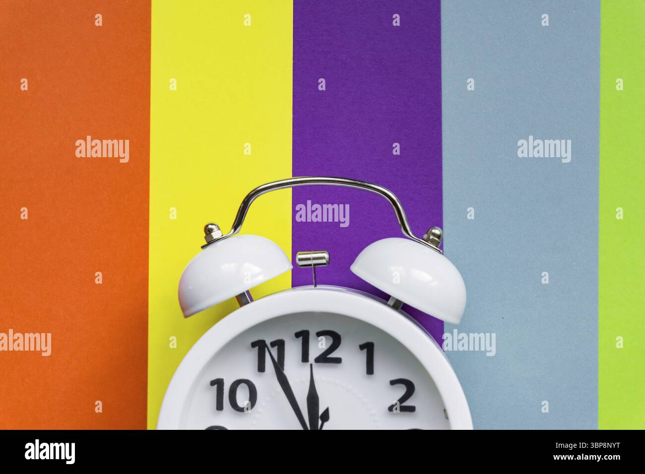 Weißer Wecker auf mehrfarbig gestreiftem Hintergrund mit Kopierraum für Text Stockfoto