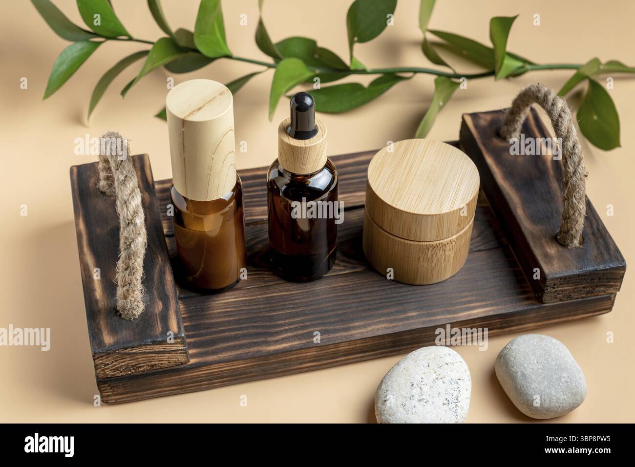 Modell mit KOSMETIKARTIKELN IM SPA-Bereich. Kosmetikflaschen und -Gläser aus dunklem Glas mit Holztablett auf beigem Hintergrund. Natürliches organisches Beauty-Produktkonzept, M Stockfoto