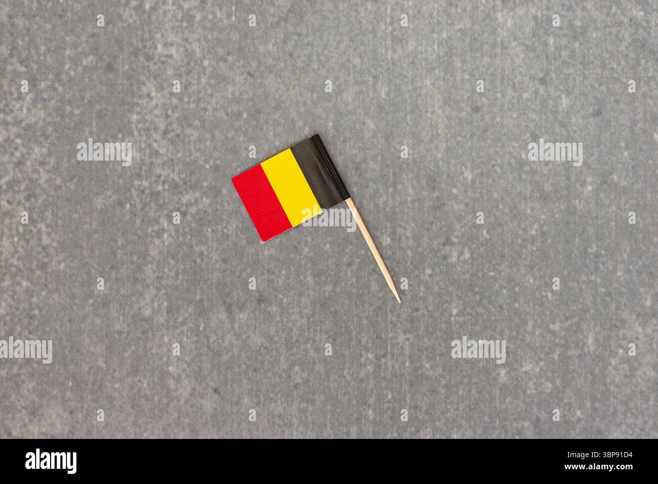 Mini Belgien Flagge auf Stock vor grauem Hintergrund Stockfoto