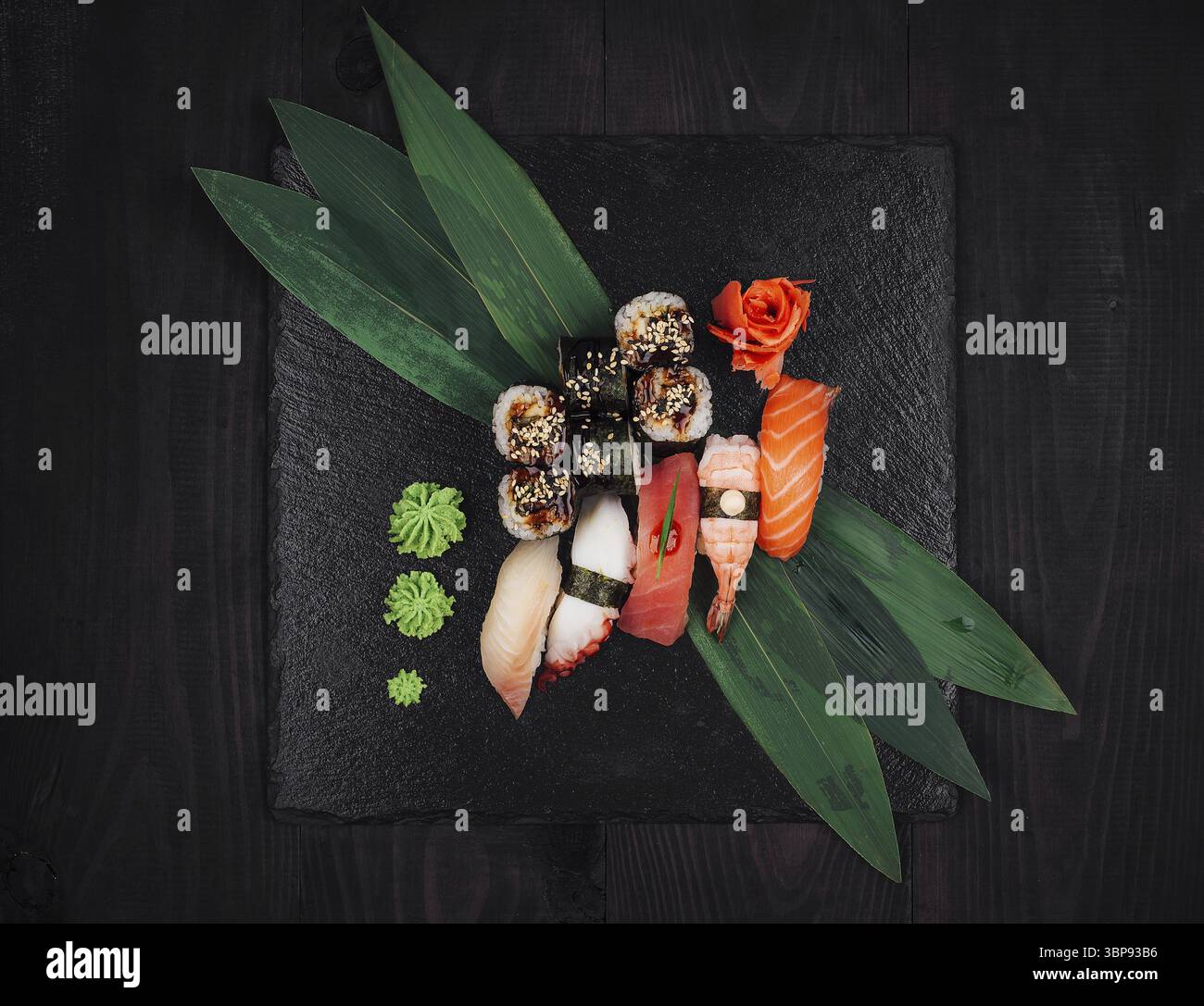 Essen, frisches Sushi wird auf einem schwarzen Schiefer mit Wasabi, Ingwer und Bambusblättern serviert Stockfoto