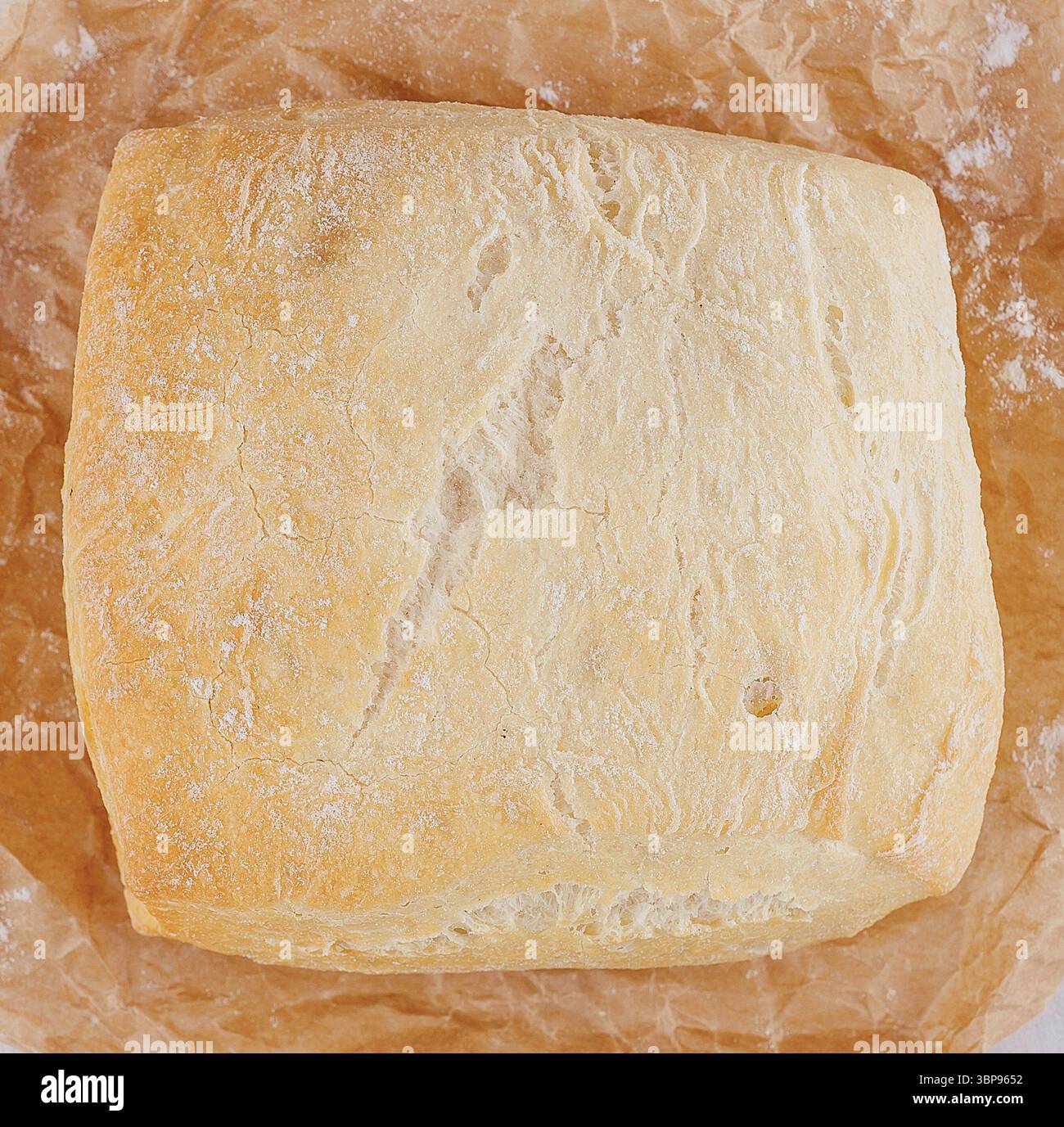 Essen, frisch gebackenes Brot, das auf braunem Backpapier auf weißem Holztisch mit Mehl bestreut ist Stockfoto