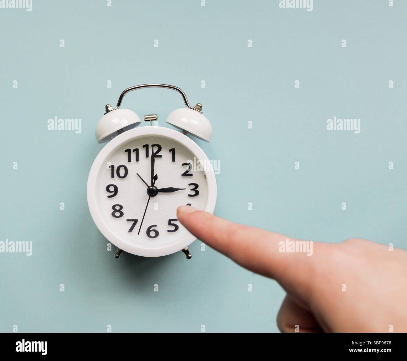 Weibliche Hand, die auf weißen Wecker zeigt. Termin und Geschäftskonzept Stockfoto