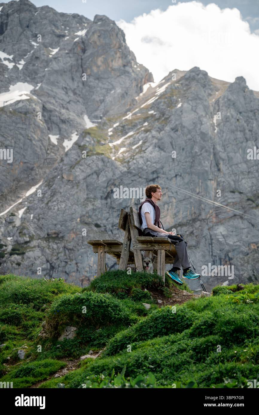 Mann, der auf einer Holzbank mit Hund darunter in den österreichischen Alpen ruht Stockfoto