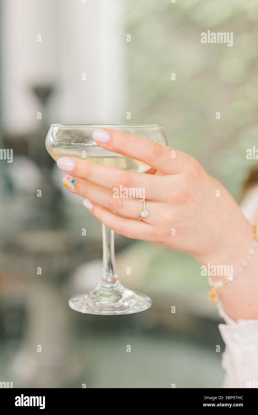Womanâ Hand mit Verlobungsring mit Champagner-Coupé Stockfoto