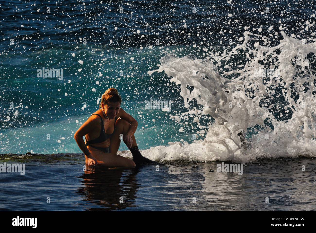 Attraktive Frau im Badeanzug, die sich während des Sonnenuntergangs am natürlichen Swimmingpool entlang der Küste entspannt, Charco de Isla Cangrejo, Teneriffa, Kanarische Inseln, Spanien Stockfoto