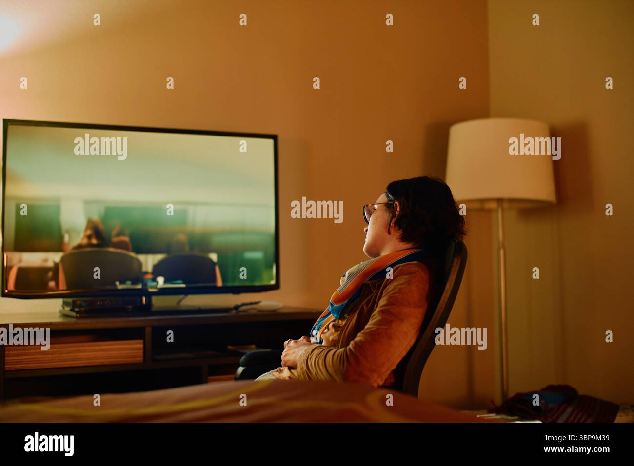 Person, die in einem schwach beleuchteten Raum auf einem Stuhl mit einer Stehlampe in der Nähe Fernsehen kann. Los Angeles, USA Stockfoto