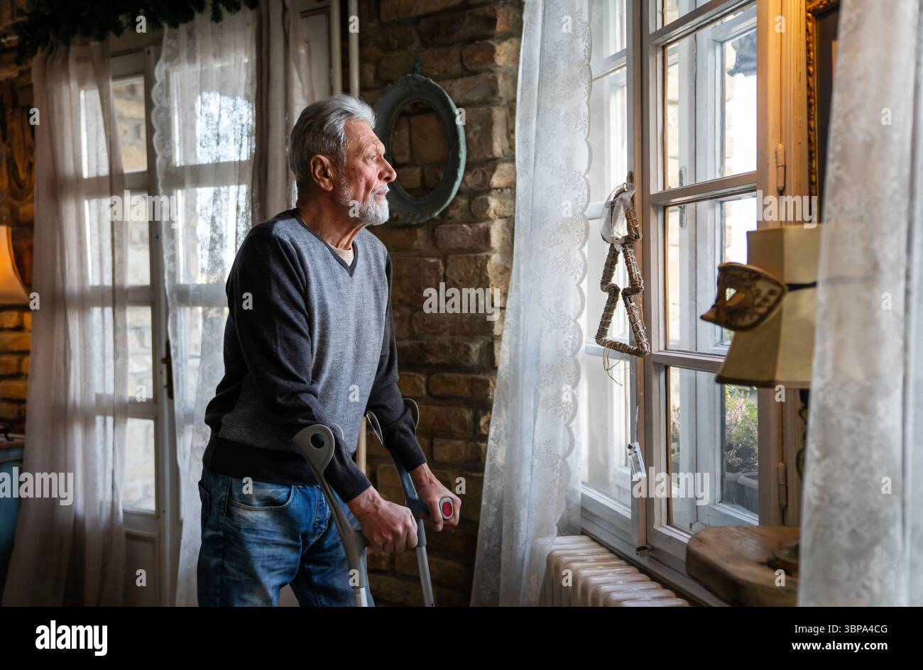 Ein alter Mann mit Krücken, der sich enttäuscht fühlt, in traurigen Gedanken allein zu Hause verloren. Witwe reifer Mann. Stockfoto