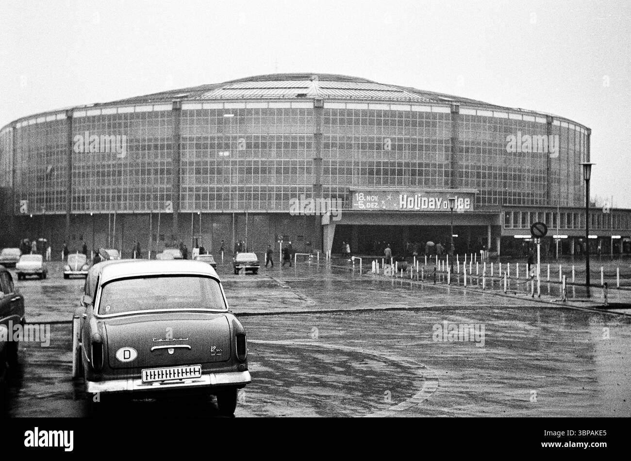 60er Jahre, 04.12.1965, Deutschland, Dortmund, Ruhrgebiet, Westfalen, Nordrhein-Westfalen, NRW, Westfalenhallen Dortmund, Westfalenhalle, Westfälische Säle, Messezentrum, Konferenzzentrum, Mehrzweckraum, Werbeplakat mit Hinweis auf die Veranstaltung 'Holiday on Ice', Parkplatz, Autos Stockfoto