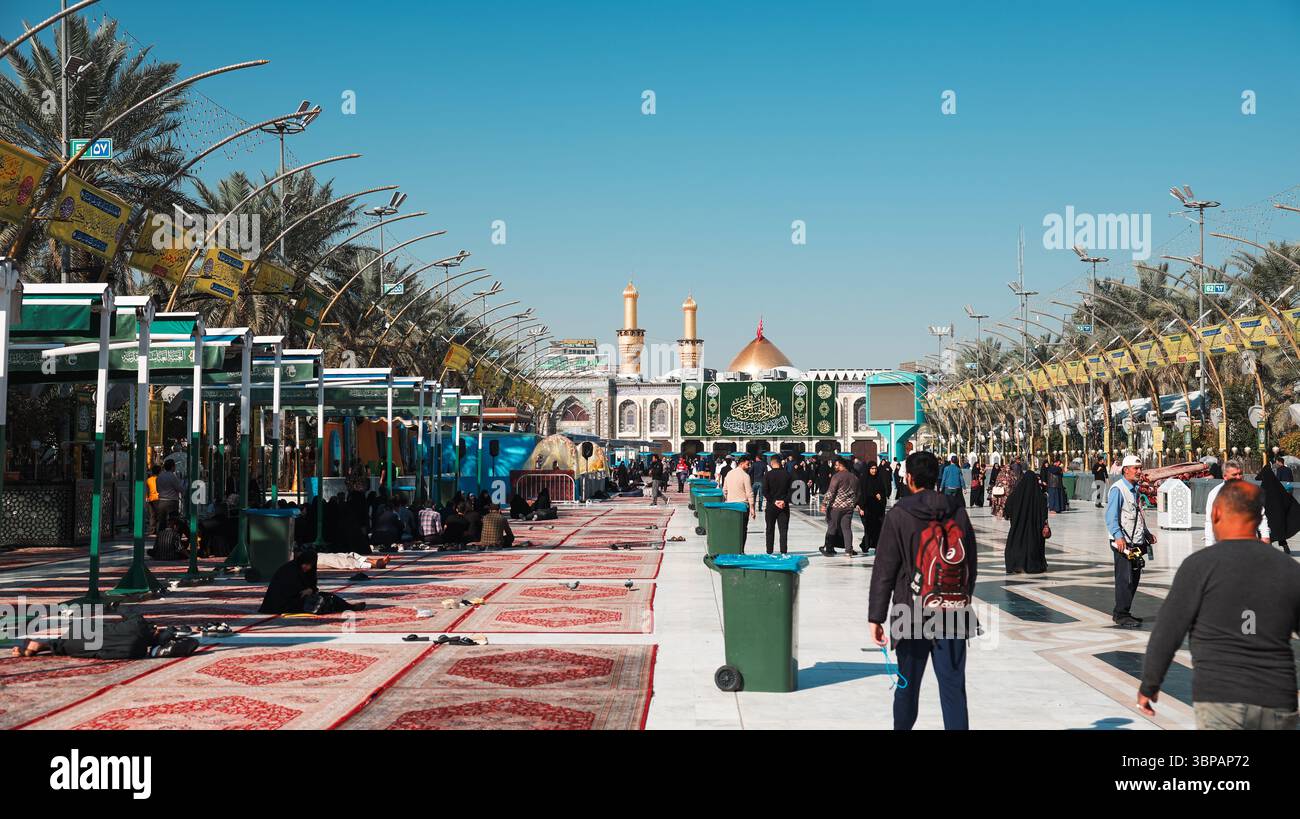 Menschenmassen erkunden die heilige Gegend in Karbala Irak unter klarem Himmel, während sie sich an verschiedenen religiösen und kulturellen Aktivitäten beteiligen. Stockfoto