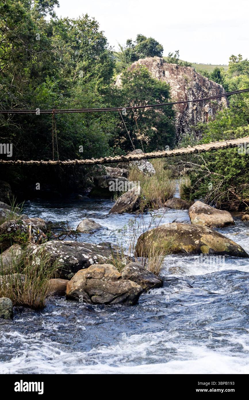 Eine kleine, wackelige Seilbrücke für Wanderer, die einen turbulenten, schnell fließenden Fluss im Royal Natal National Park in den Drakensbergen überquert Stockfoto